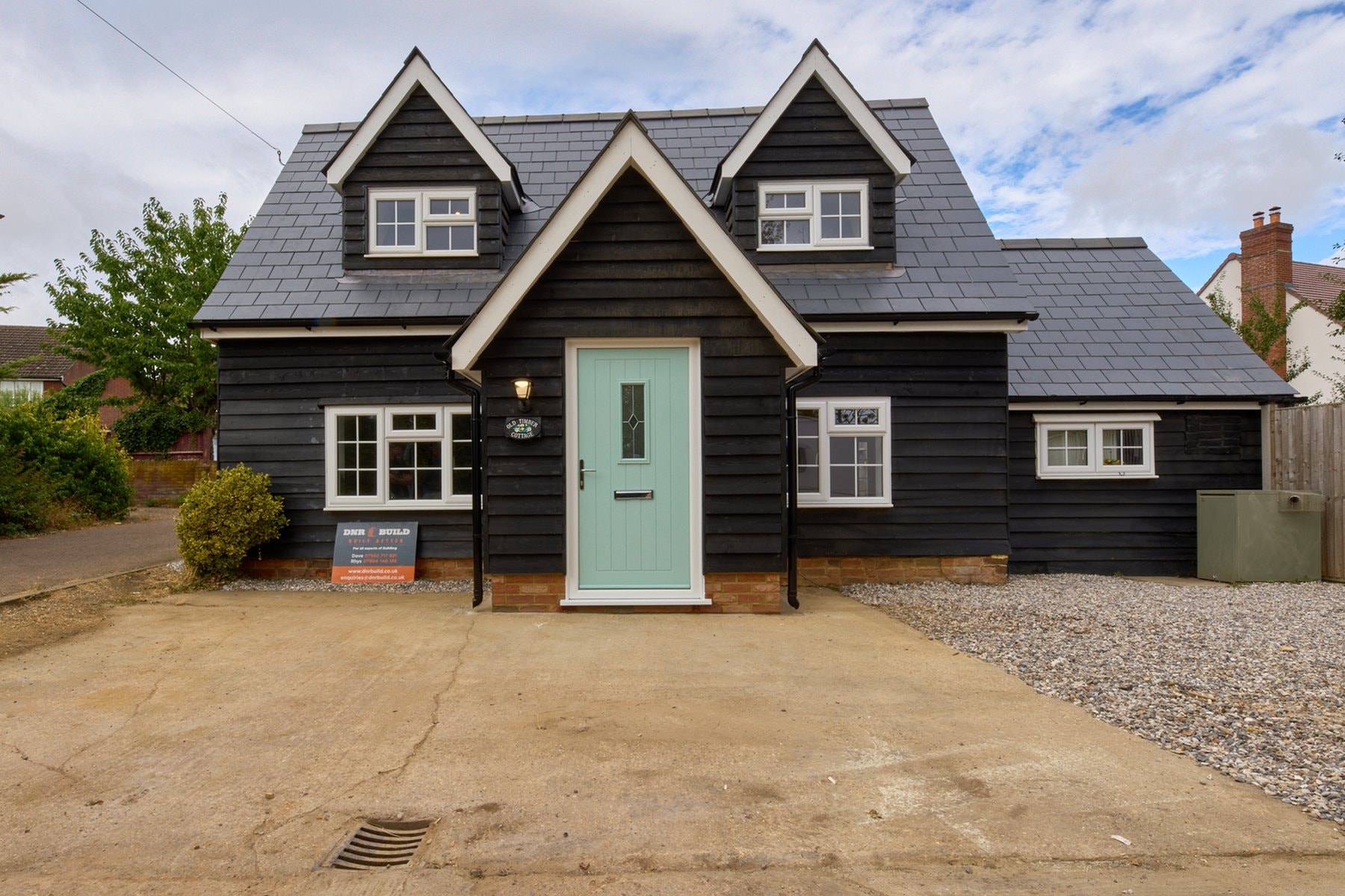 The front of the Old Timber Cottage after the renovation by DNR Build, with a new roof, black weatherboarding and a sage green front door